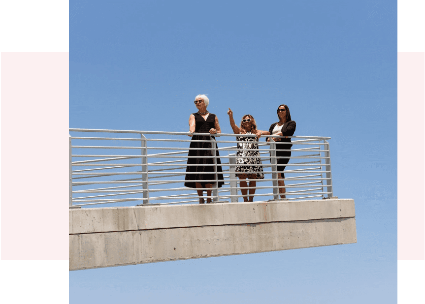 Three women standing on a bridge with one waving.